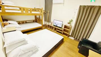 A hotel room with a bunk bed, a flat bed, a television, a small desk, and a plant.