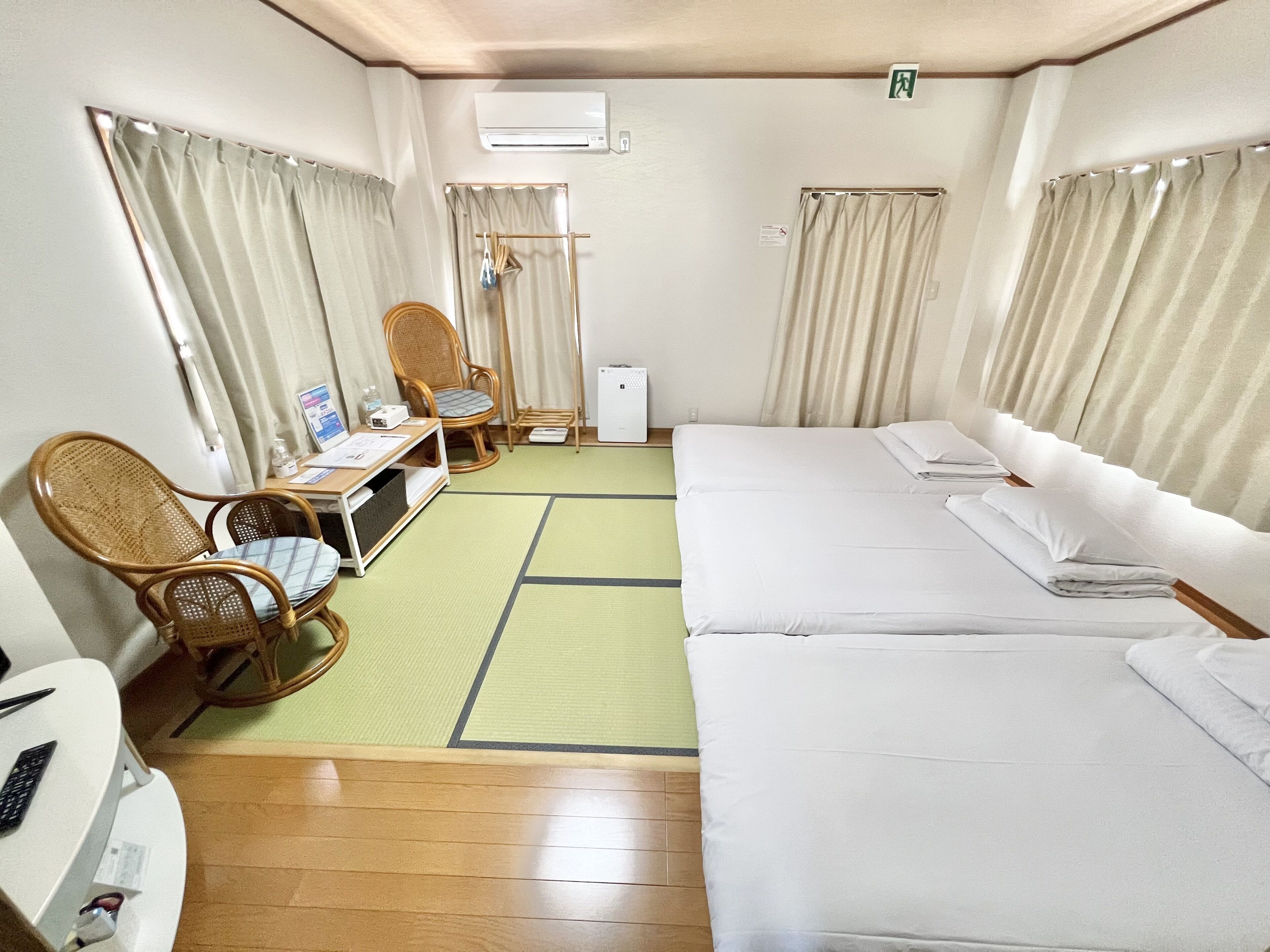 Hotellihuone, jossa on kaksi sänkyä, työpöytä, jossa on tietokone, tuoli ja pieni pöytä.