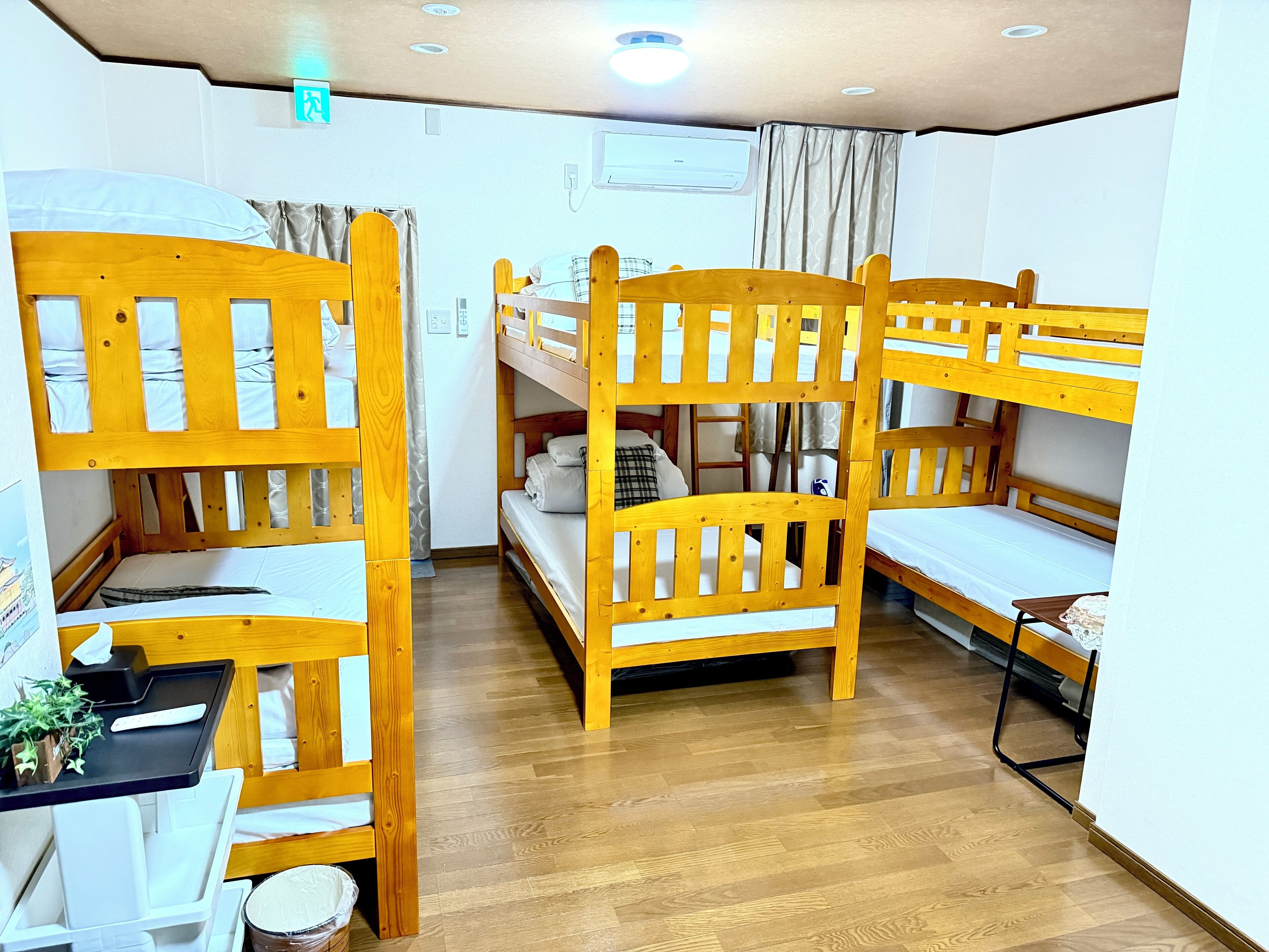 A room with bunk beds, a small desk with a chair, a trash bin, and a window with curtains.