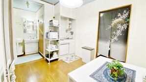A compact kitchen with white appliances, a small dining table, and a decorative plant. - Petit Hotel 017 (Tokushima)