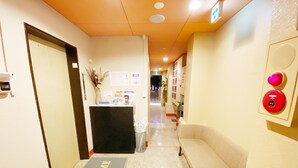 A hotel reception area with a reception desk, a welcome mat, a sofa, and a wall-mounted intercom system. - Petit Hotel 017 (Tokushima)