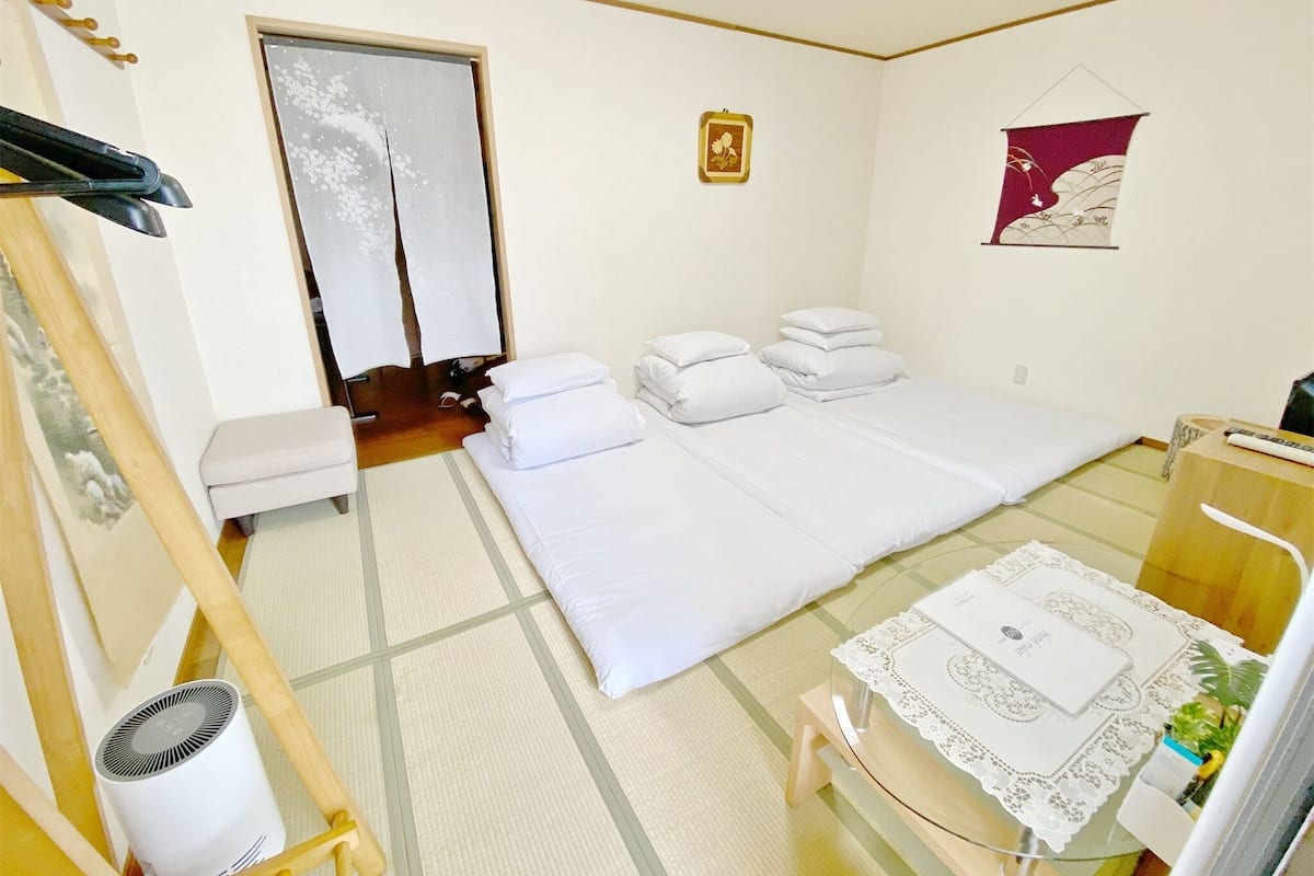 A hotel room with a bed, a small table with a tablecloth, a chair, a heater, and a wardrobe.
