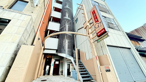 A hotel entrance with a modern design, featuring a curved staircase leading to the entrance, a large vertical sign, and a clear view of the sky. - Petit Hotel 017 (Tokushima)