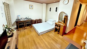 A hotel room with a bed, a desk, a chair, a mirror, a clock, and a small table with a vase of flowers. - Petit Hotel 017 (Tokushima)