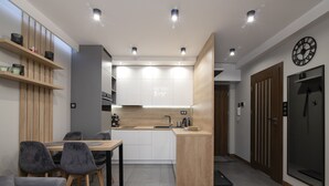 A modern kitchen with white cabinets, a wooden countertop, and a built-in oven. There is a dining area with a table and chairs, and a sofa in the foreground. - Apartamenty Sun & Snow Spokojna (Wisla)