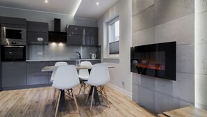 A modern kitchen with built-in appliances, a dining area with white chairs, and a large flat-screen TV mounted on the wall. - Apartamenty Sun & Snow Spokojna (Wisla)
