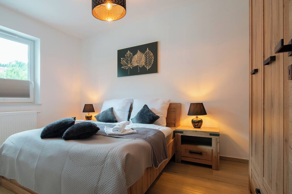 A bedroom with a bed, two bedside tables, a window, and a wall-mounted artwork.