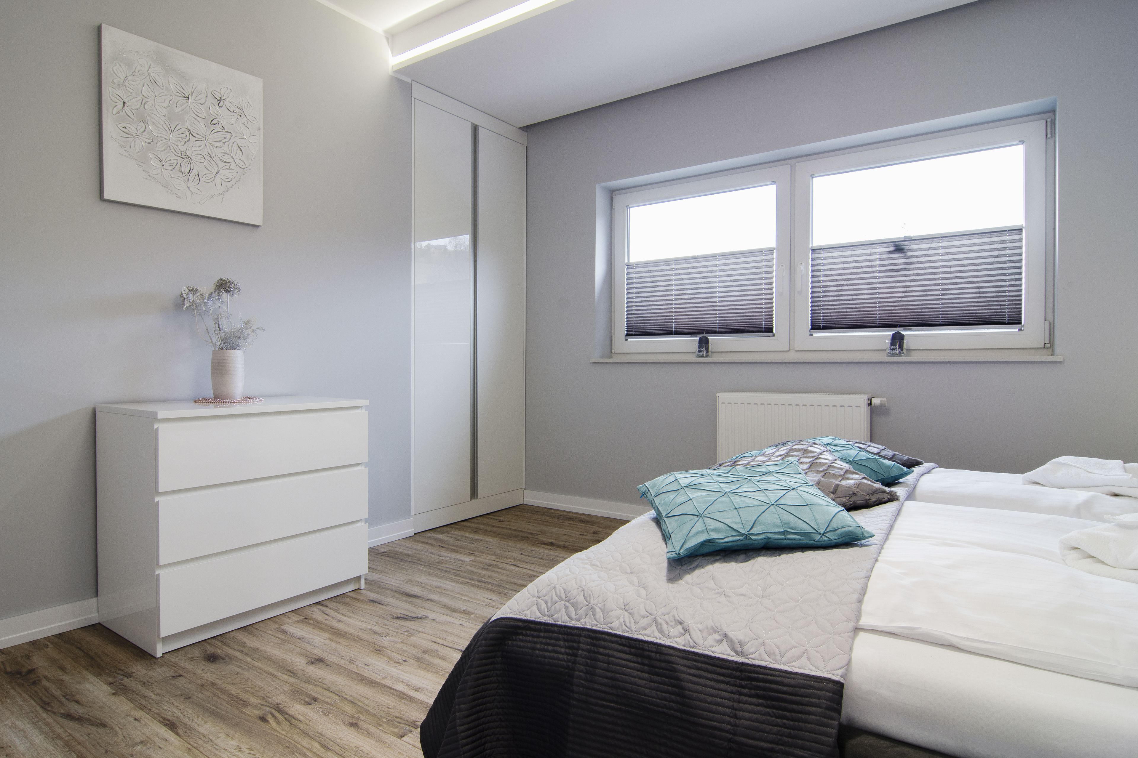 A bedroom with a bed, a dresser, a radiator, and a window with blinds.