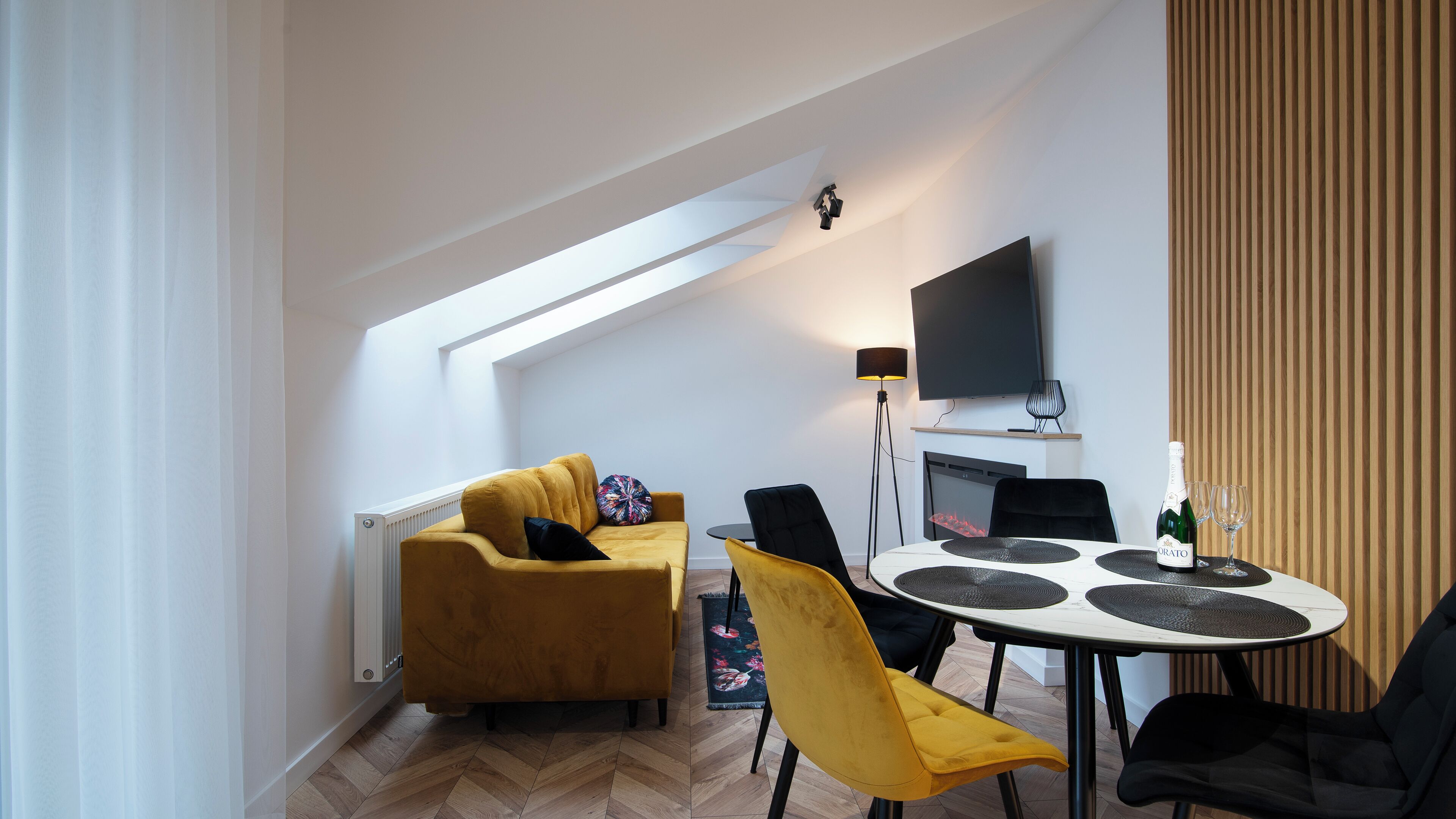 A modern living room with a sofa, chairs, a dining table, and a TV mounted on the wall.