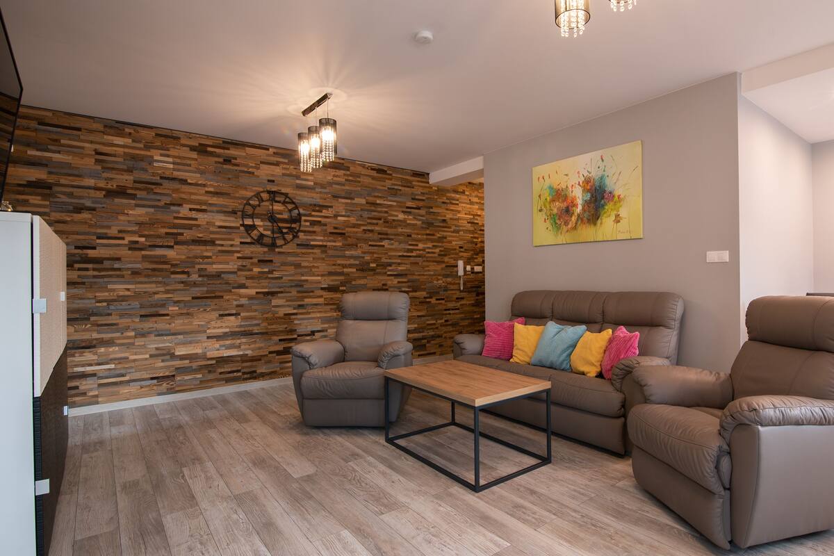 A modern living room with a wooden accent wall, a sofa set, a coffee table, and a painting.
