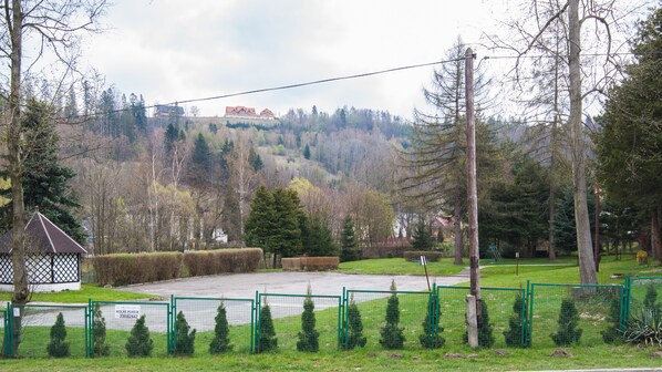 A fenced outdoor area with a small pavilion, a grassy field, and a hill with buildings in the background. - Sun & Snow Spokojna (Wisla)