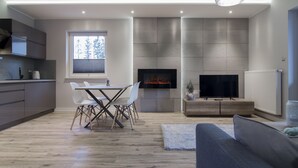 A modern living room with a fireplace, a television, and a dining area with chairs and a table. - Apartamenty Sun & Snow Spokojna (Wisla)