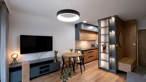 A modern living room with a flat-screen TV, a round dining table, and a built-in bookshelf. - Apartamenty Sun & Snow Spokojna (Wisla)