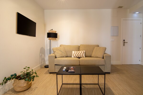 Una sala moderna con un sofá color beige, una mesa de centro negra y una lámpara de pie.