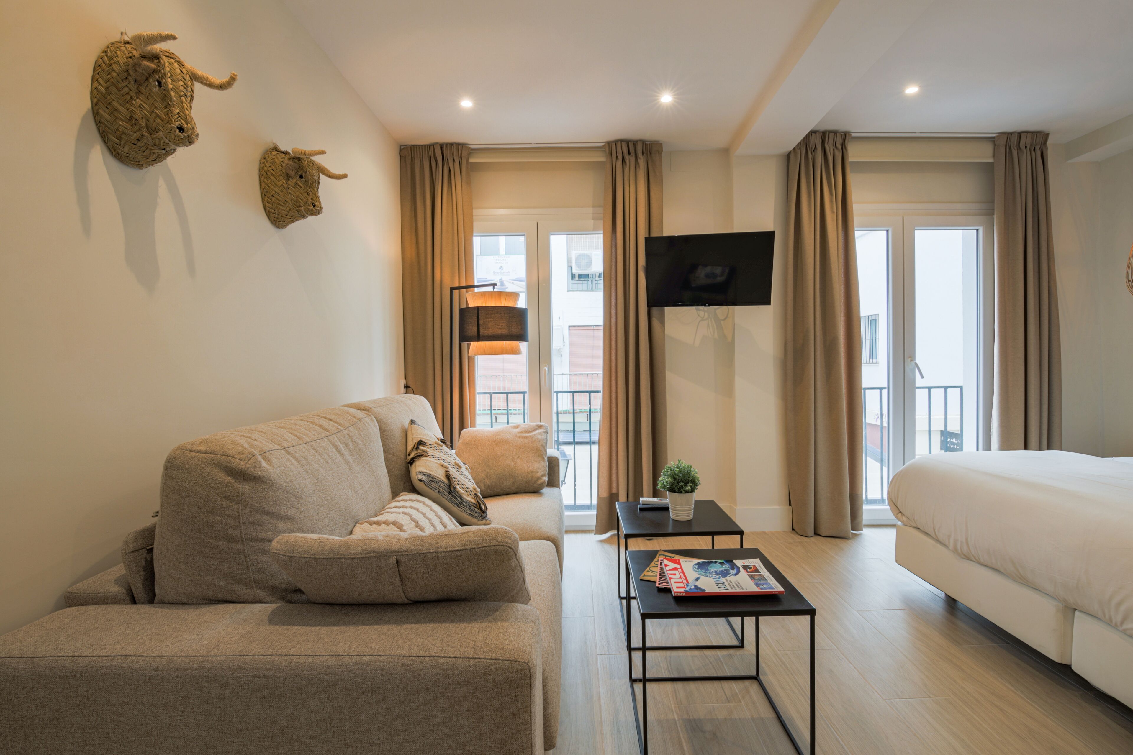 Une chambre d’hôtel moderne, équipée d’un canapé, d’une petite table avec un magazine, d’un lit et d’un téléviseur fixé au mur.