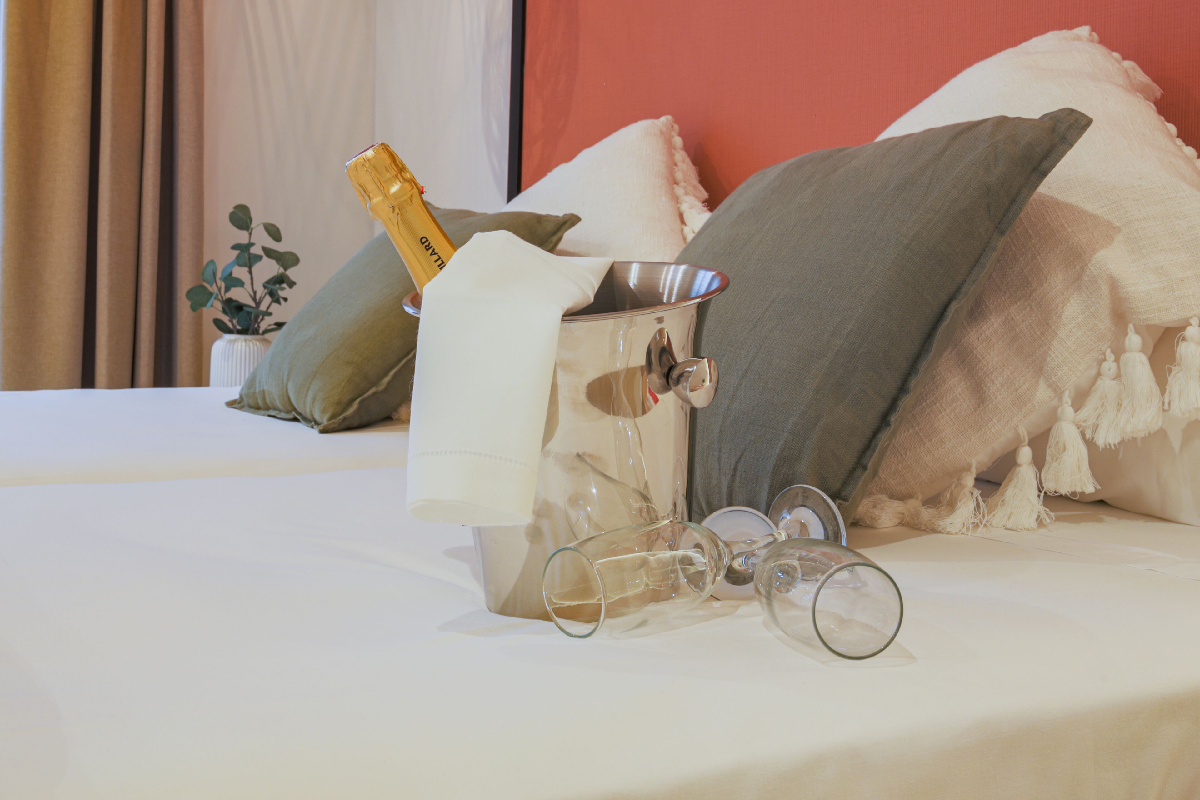 Una cama con una botella de champán, copas y un recipiente metálico encima.