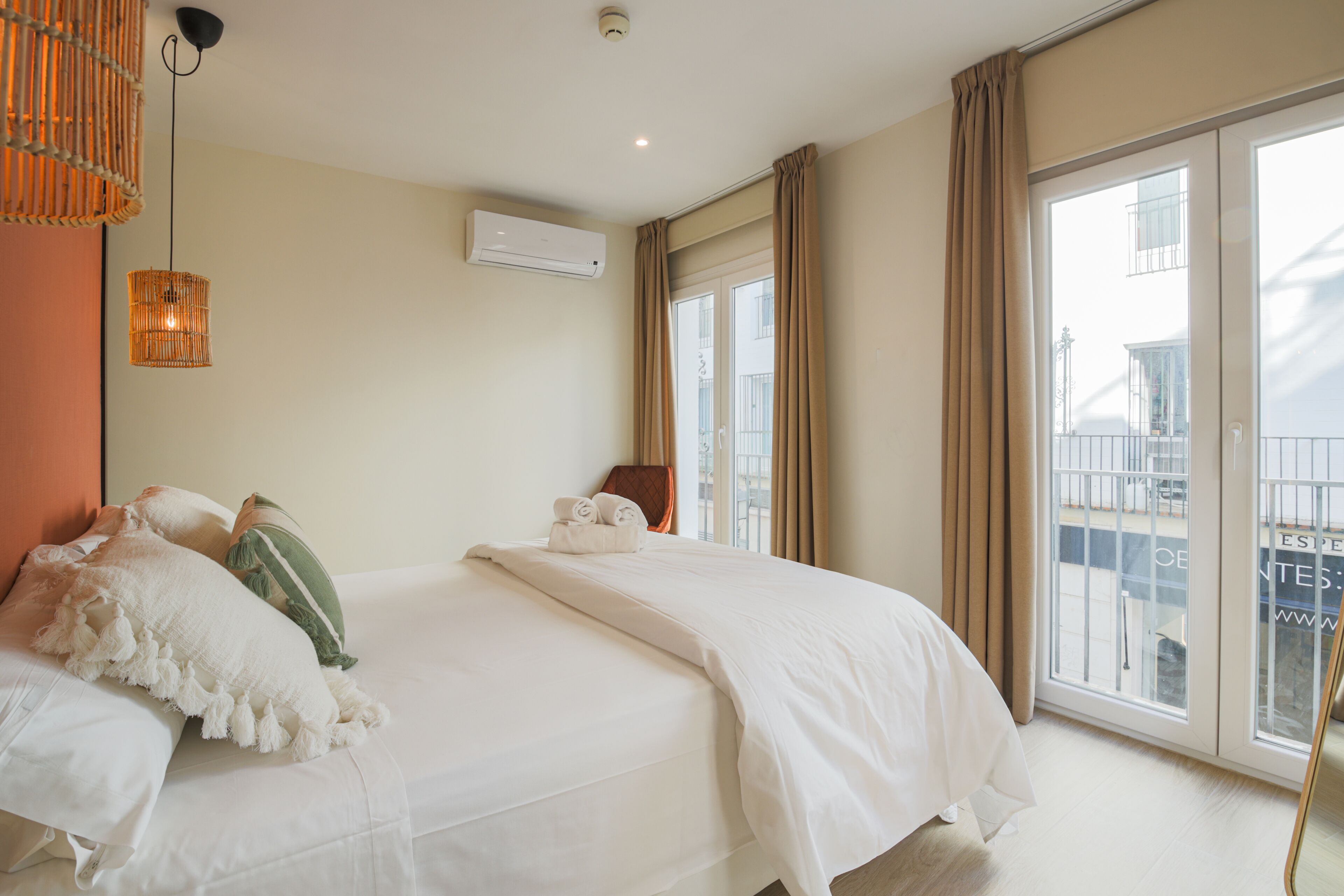 Une chambre d’hôtel avec un grand lit, une fenêtre avec des rideaux, un appareil de climatisation et un luminaire suspendu.
