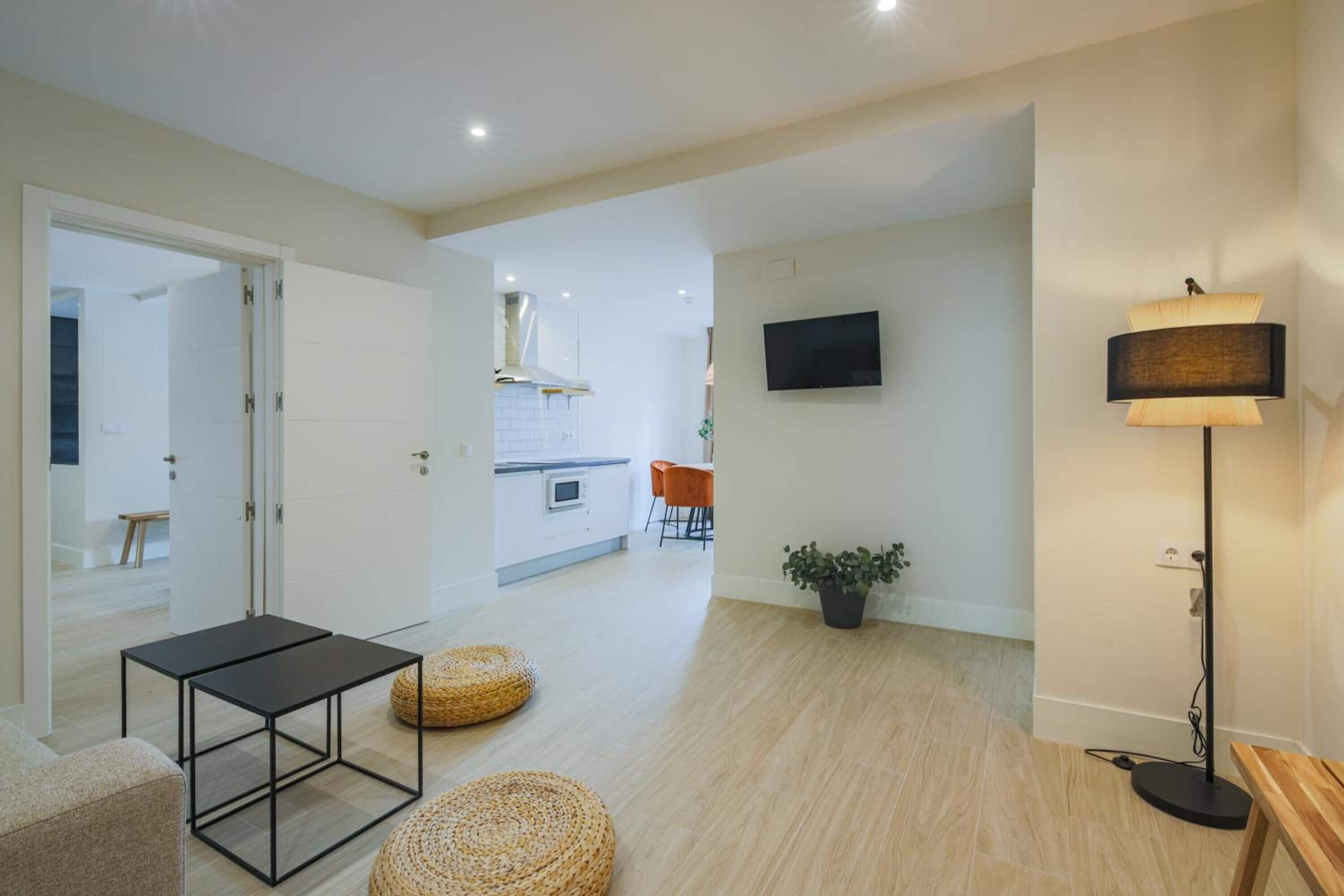 A modern living room with a sofa, a small table, two woven poufs, a floor lamp, and a TV mounted on the wall.