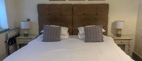 A neatly made bed with a tufted headboard, two bedside tables with lamps, and three framed pictures on the wall.