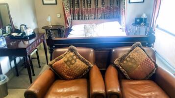 Une chambre d’hôtel avec un lit, deux fauteuils en cuir, un bureau en bois, une lampe et une fenêtre ornée de rideaux à motifs.
