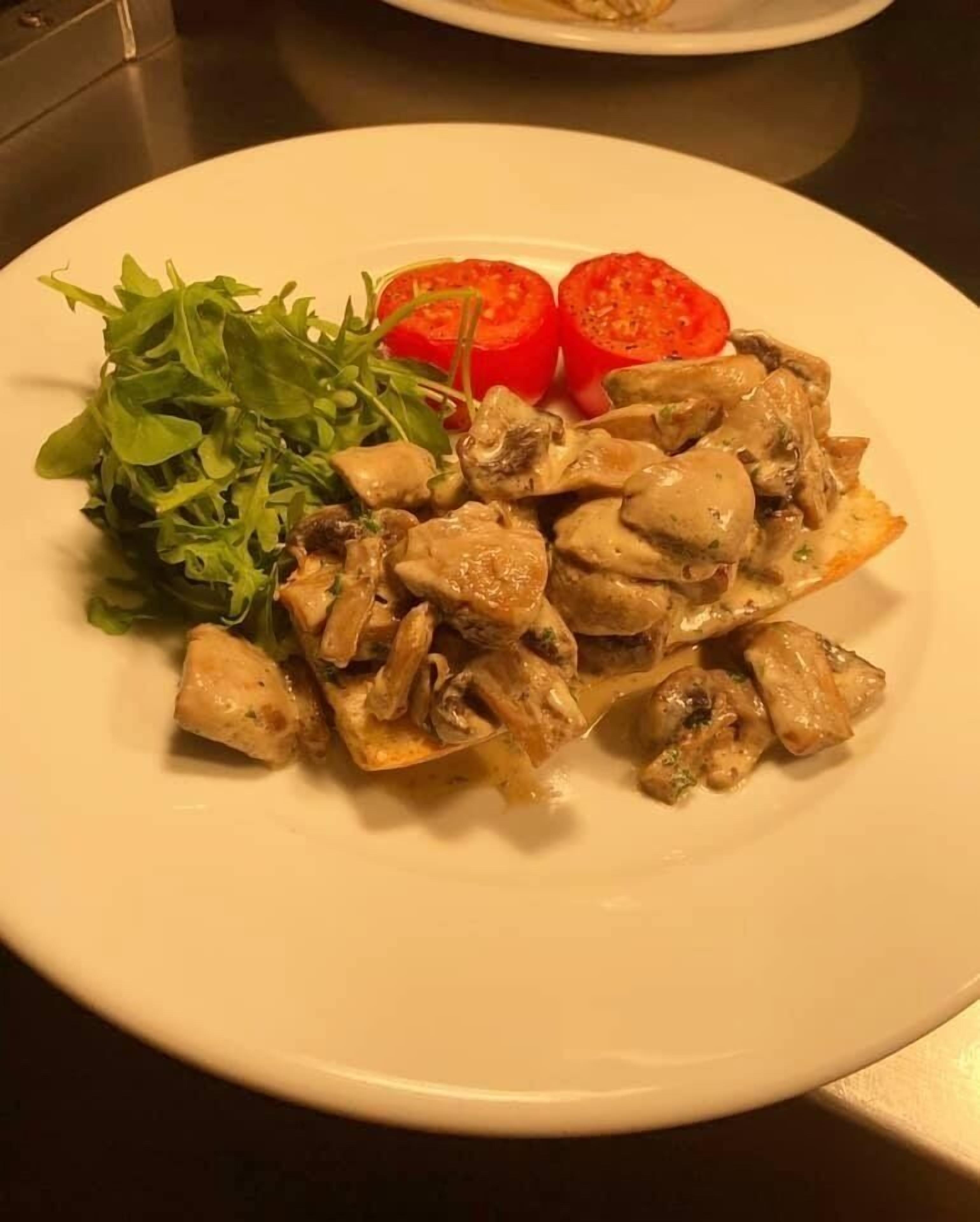Une assiette de poulet et de champignons, accompagnée d’une salade de roquette et de tomates en tranches.