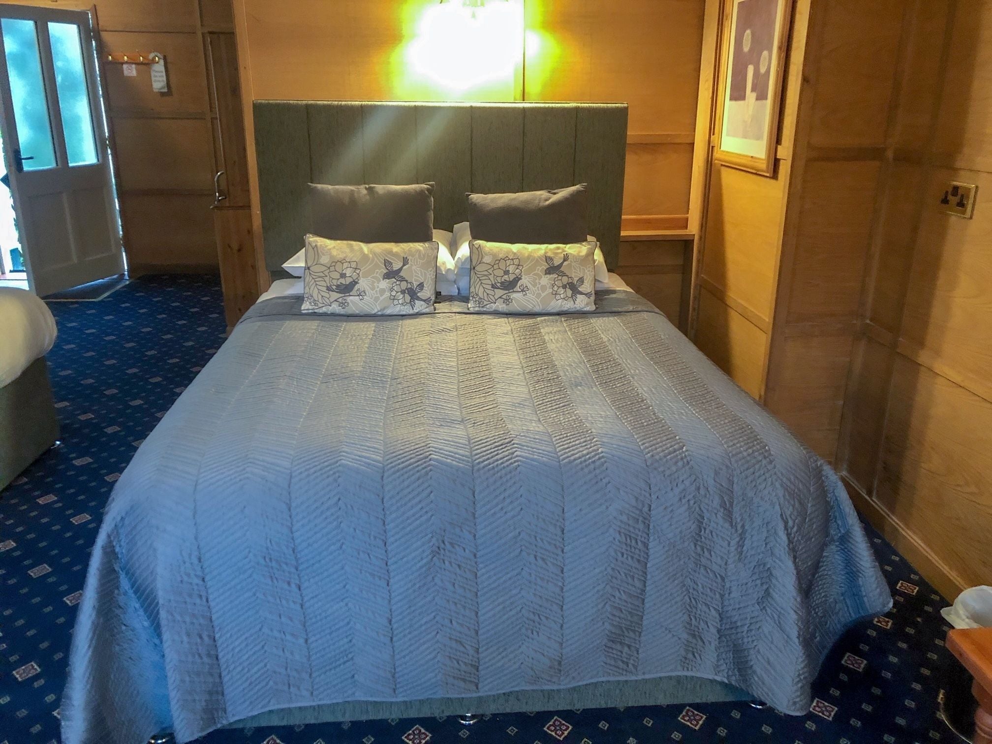 A hotel room with a large bed, a headboard, and a blue carpet.