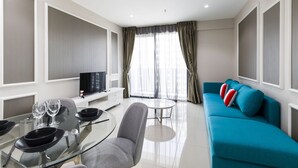 A modern living room with a glass dining table, grey sofa, and a TV on a white cabinet. - Luxury Suite Icity Shah Alam (Shah Alam)