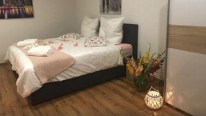 A neatly made bed with pillows and a blanket, a vase with flowers, and a lit lantern on the floor. - Oftersheim Apartment (Oftersheim)