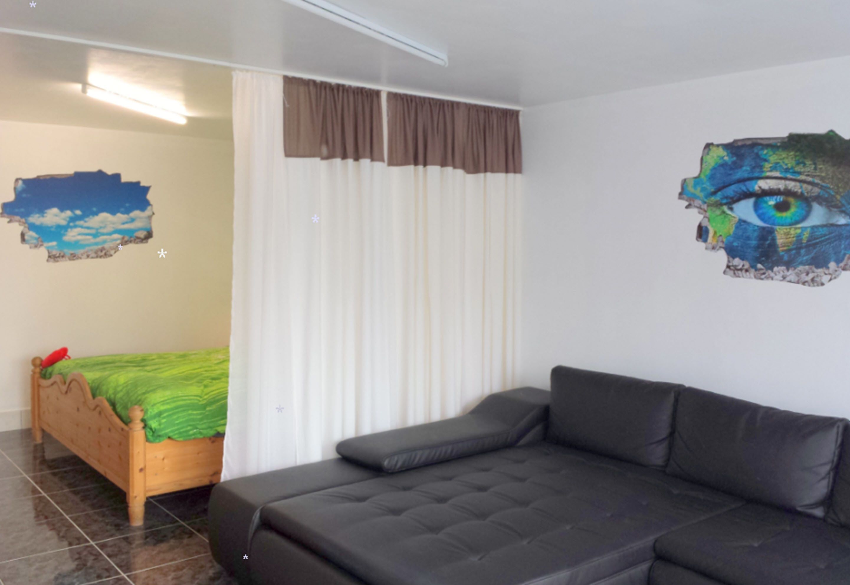 Une pièce avec un lit, un canapé, un rideau et un mur orné d’un tableau.