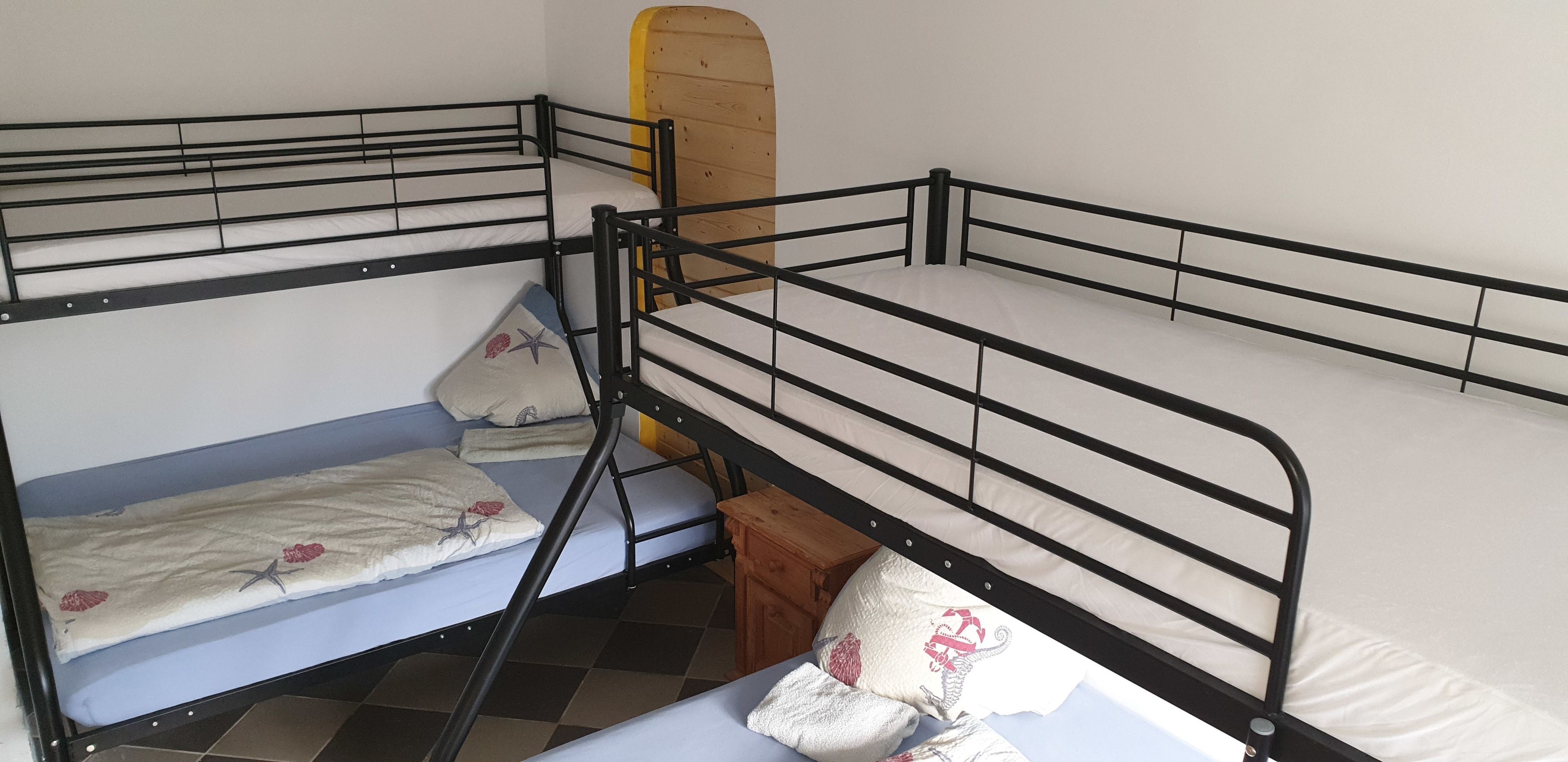 Una cama litera con escalera de madera, un taburete pequeño de madera y un almohadón con diseño floral.