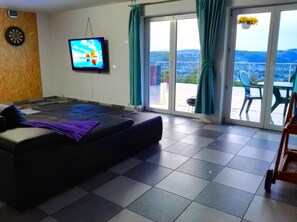 A room with a bed, a television, a dartboard, and a view of the outdoors.