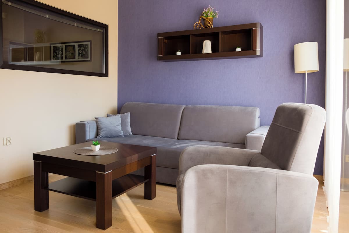 Una sala moderna con un sofá gris, una mesa de centro de madera oscura y un sillón gris claro.