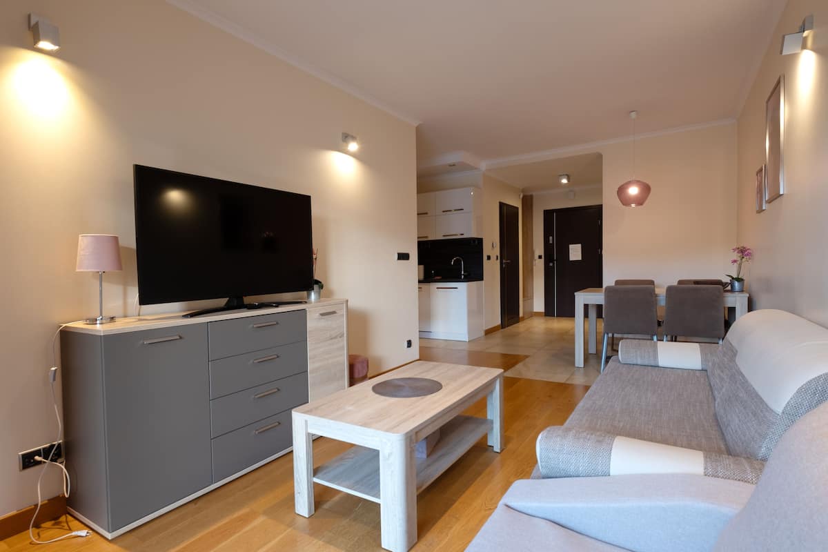 Una sala de estar moderna con un televisor de pantalla plana, un sofá gris y un comedor con mesa y sillas.