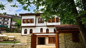 Ein zweistöckiges Gebäude mit einer Stein-Fassade, Holzläden und einem Schild, auf dem 'Hotel Emini Efendi Konak' steht.