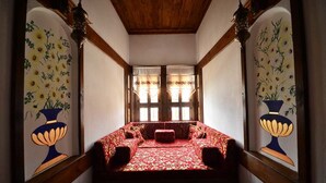 Ein schmales Zimmer mit einer rot gemusterten Couch, Holzbalken und blumengemusterten Wandverzierungen.