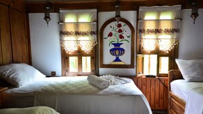 Una habitació amb dos llits, parets de fusta, un gran finestral amb una pintura floral i un penjol.