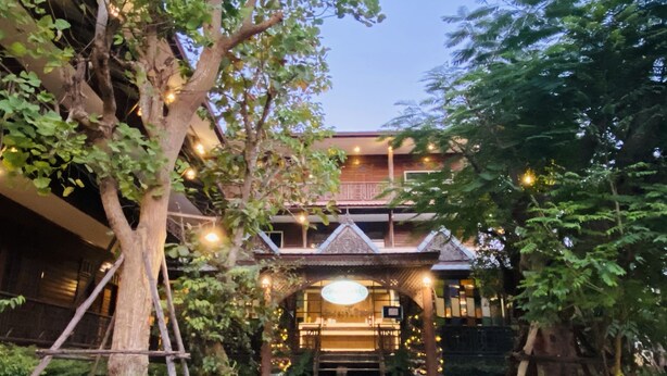 A traditional building with a central staircase and a covered entrance, surrounded by lush greenery and trees.