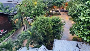 A courtyard with a wooden building, lush greenery, and a view of distant mountains.