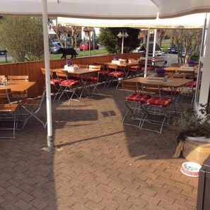 An outdoor patio with brick flooring, wooden tables and chairs, and a covered area. - Restaurant & Pension Wirtamberg (Jena)