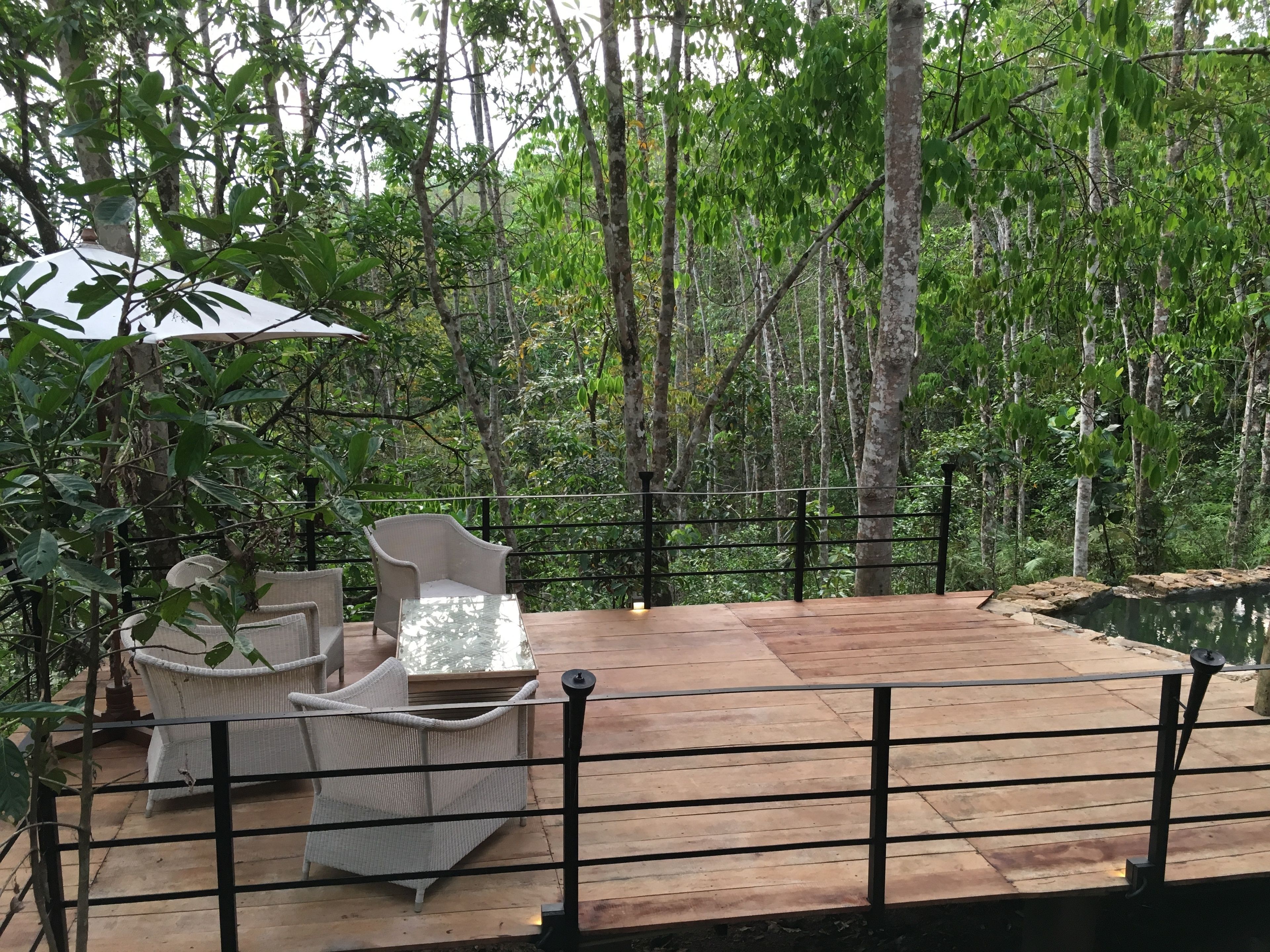 Une terrasse en bois, agrémentée de meubles en osier et d’une table en verre, le tout entouré d’une rambarde en métal.