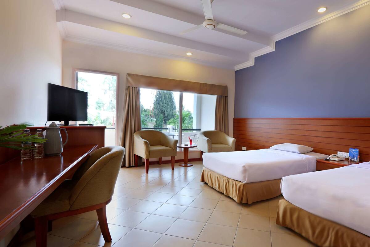 A hotel room with two beds, a desk, a chair, a TV, and a window with curtains.