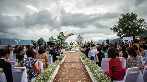 An outdoor wedding ceremony with guests seated on white chairs, a wooden aisle, and floral decorations. - Niagara Hotel Lake Toba & Resorts (Parapat)