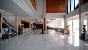 A spacious lobby with a high ceiling, a staircase on the left, and a large window on the right. - Niagara Hotel Lake Toba & Resorts (Parapat)