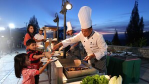 A chef preparing food at an outdoor cooking station with a view of the evening sky. - Niagara Hotel Lake Toba & Resorts (Parapat)