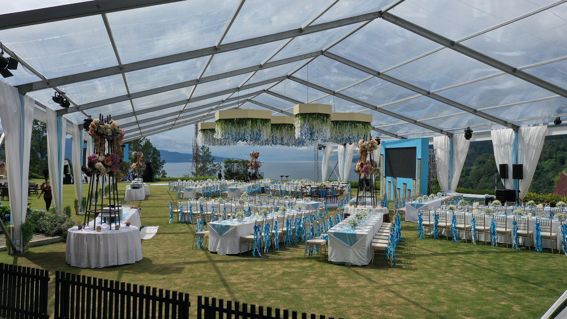A tented event space with tables set for a reception, overlooking a scenic landscape.