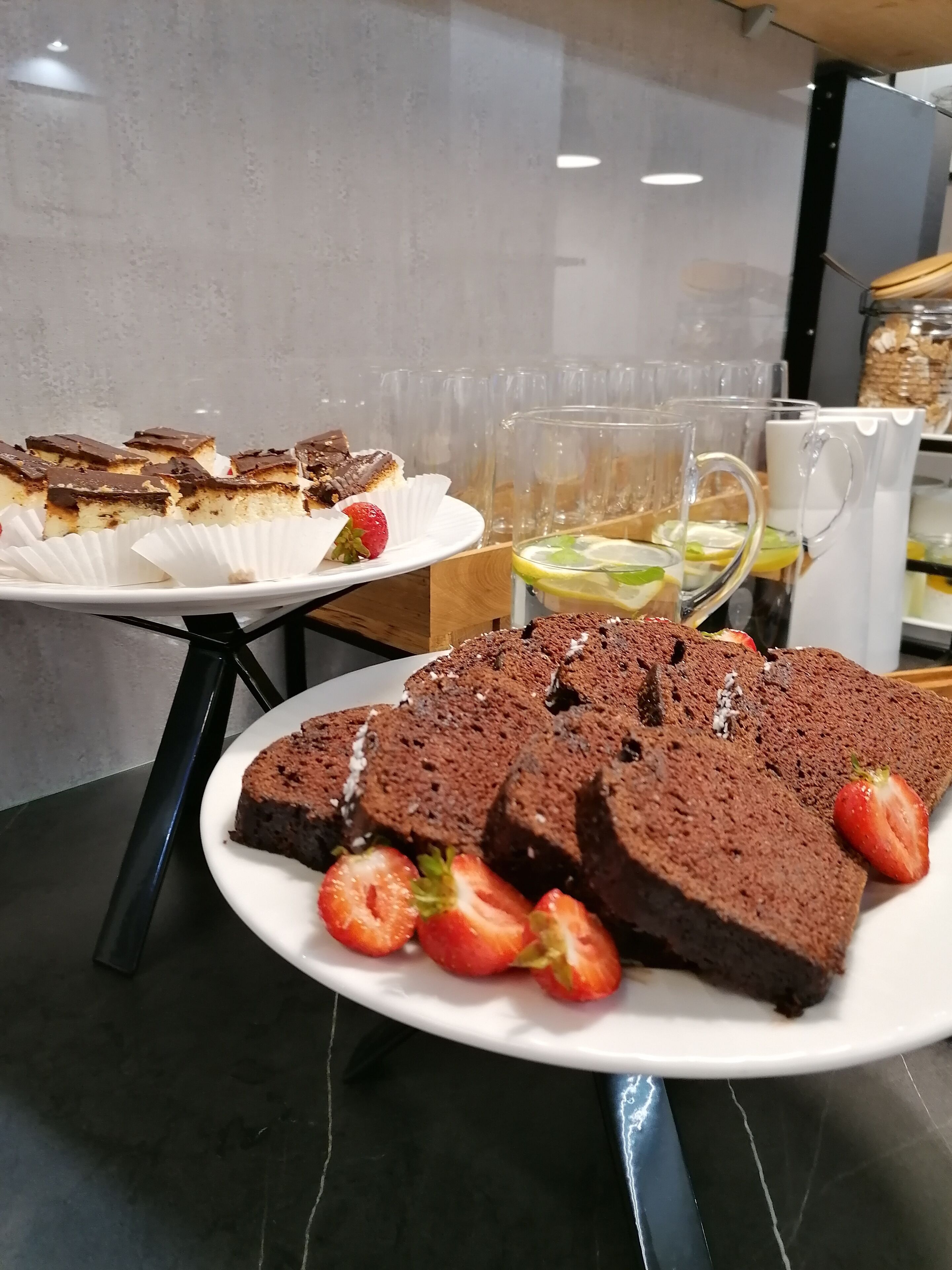A dessert display with various cakes and a pitcher of iced tea.