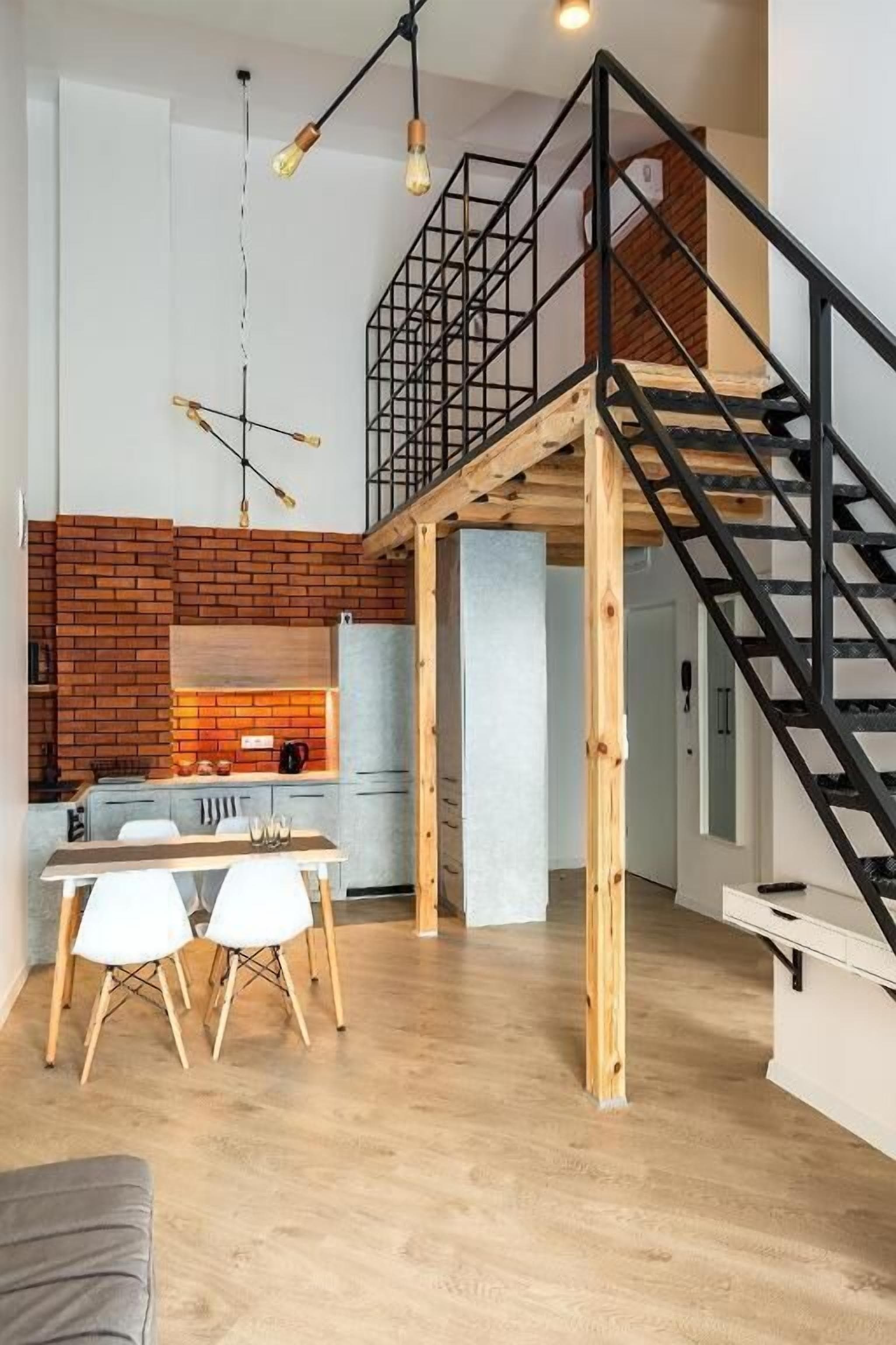 A modern loft with exposed brick walls, a wooden dining table, and a black metal staircase.