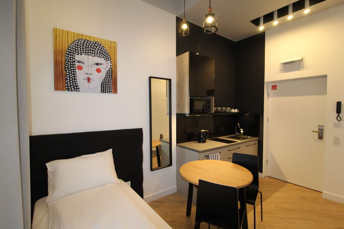 A hotel room with a bed, a dining table with chairs, a kitchen area, and a large mirror.