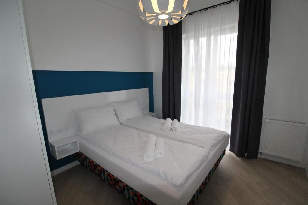 Ett modernt hotellrum med en stor säng, ett nattduksbord och ett fönster med gardiner.