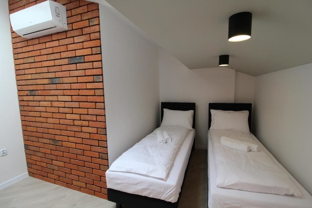 Una habitación pequeña y moderna con dos camas individuales, una pared de ladrillo y un aire acondicionado instalado en el techo.